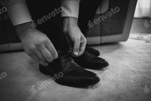 Preview: Grayscale shot of a man tying his leather shoes