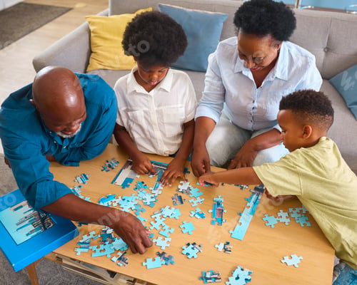 Preview: Grandparents With Grandchildren Indoors Sitting Around Table At Home Doing Jigsaw Puzzle Together