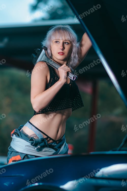 Preview: Attractive young female as an auto mechanic working with a wrench in garage