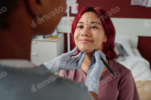 Preview: Smiling teenager looking at female plastic surgeon drawing liftmarks