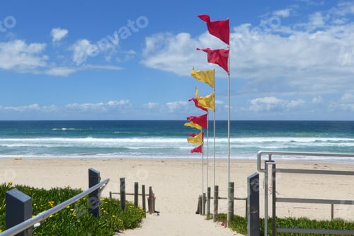 Preview: Red and yellow flags at the beach path leading towards water