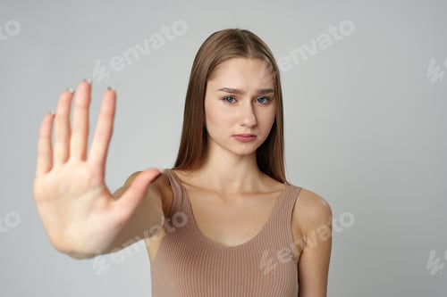 Preview: Young Woman in Fashionable Outfit Standing Against a Neutral Backdrop Showing Stop Gesture