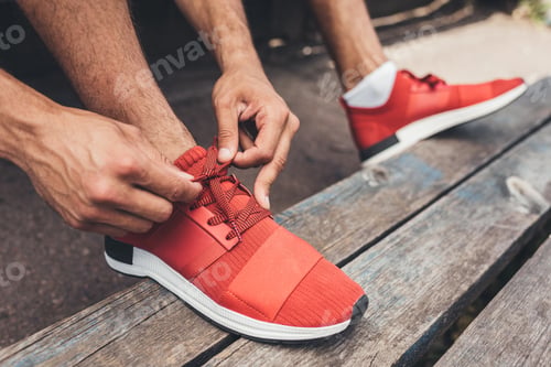 Preview: cropped shot of sportsman tying shoelaces while sitting on bench at sport playground