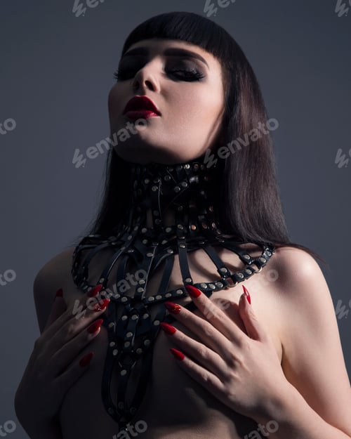 Preview: Portrait of young woman wearing ornate leather necklace, covering naked breasts with hands