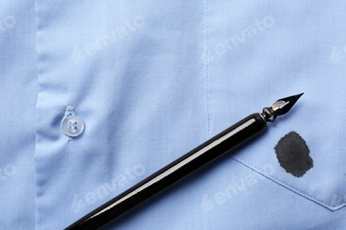 Preview: Black ink stain on light blue shirt and pen, top view. Space for text