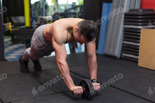 Preview: Muscular young man performing exercises with the abdominal wheel.