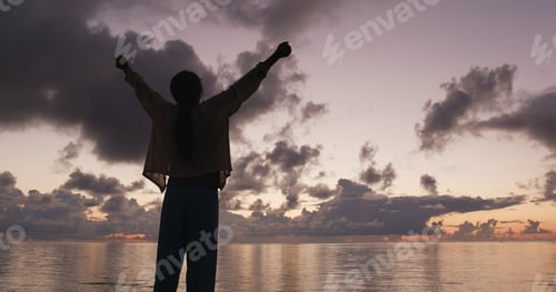 Preview: Silhouette of woman raising hand at sunrise time