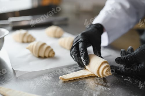 Preview: Baker making croissants in bakery: rolling dough for perfect pastry
