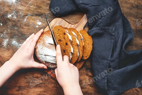 Preview: Women's hands cutting with knife rye sourdough bread with raisins, sliced pieces