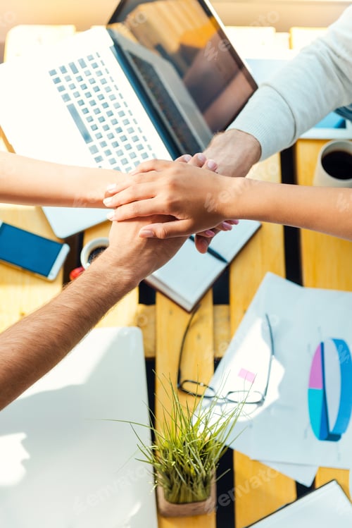 Preview: Team spirit. Top view of business people holding hands clasped upon the wooden desk