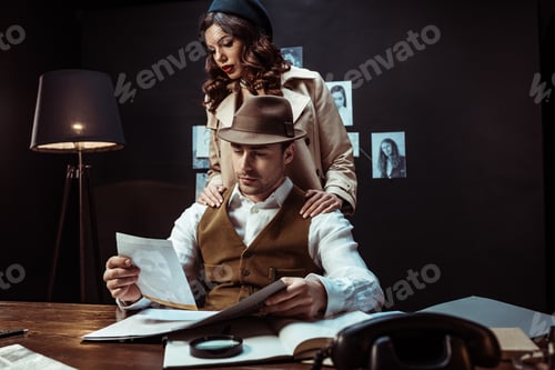 Preview: Detective and beautiful woman in trench coat looking at photo in dark office
