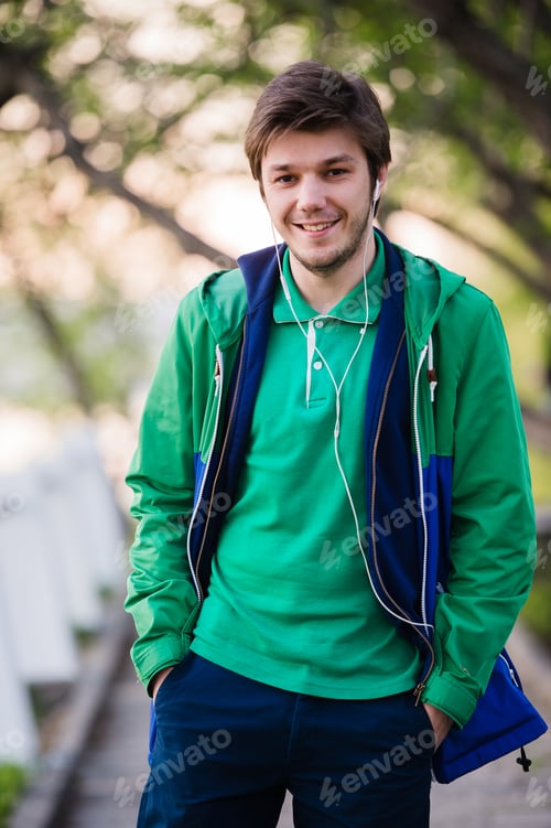 Preview: handsome man walking around the city smiling and listening to music in park. Soft sunset light.