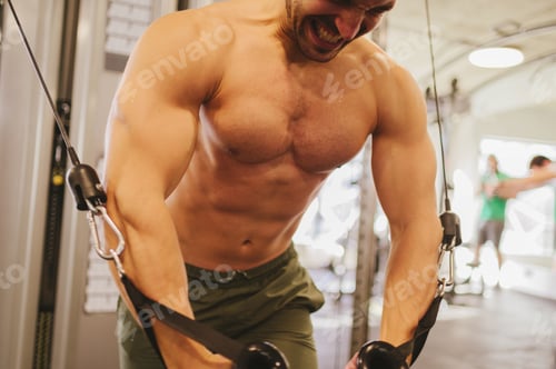 Preview: Close up of a powerful shirtless muscular weightlifter pulling weights on a cable machine in a gym.