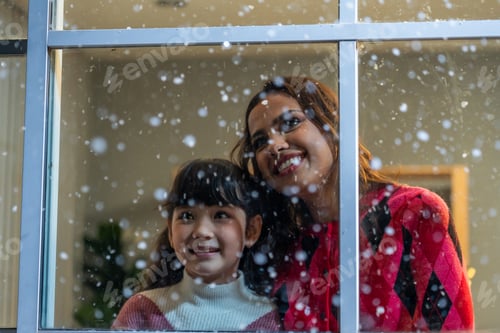 Preview: Adorable child looking at the window and admire snowflakes with mother.