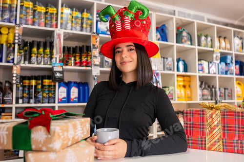 Preview: Young woman wearing an elf hat, holding a cup and smiling with gifts