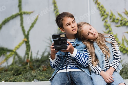 Preview: girl in denim vest and jeans leaning on shoulder of preteen boy in stylish clothes holding vintage