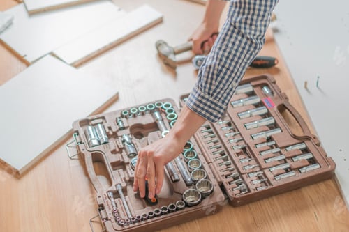 Preview: young man choobsing wrench from the tool kit on the wooden floor