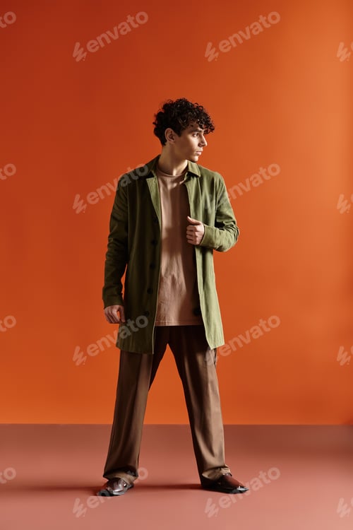 Preview: Fashionable young man showcasing stylish outfit against vibrant orange backdrop