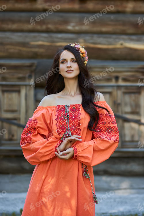 Preview: Beautiful Slavic woman in an orange ethnic dress and a wreath of flowers on her head. Beautiful