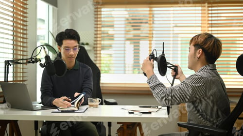 Preview: Young podcaster using a microphone and laptop computer recording audio for channel in home studio.