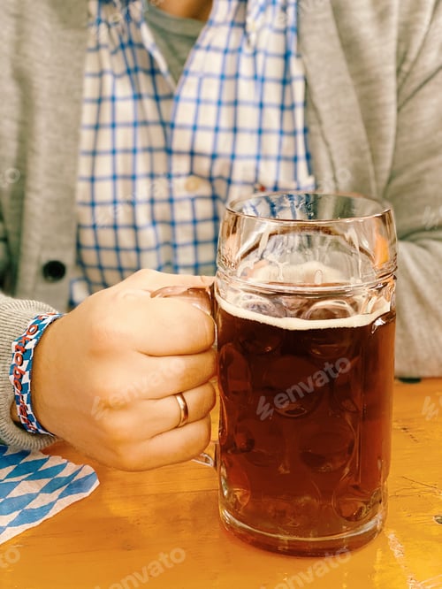 Preview: Young man holding a beer mug full of dark beer