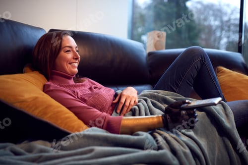 Preview: Woman With Prosthetic Arm And Hand At Home Relaxing On Sofa Watching TV