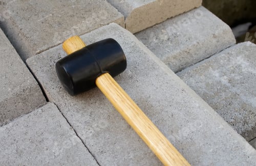 Preview: Rubber mallet with a wooden handle lying on grey concrete paving blocks