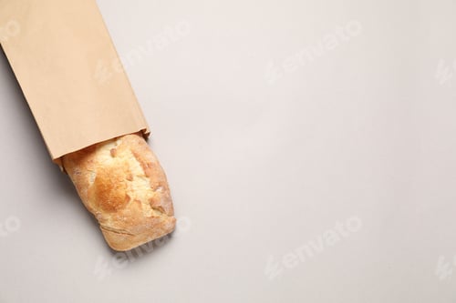 Preview: Paper bag with fresh baguette on light gray table, top view. Space for text