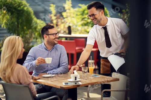 Preview: Happy waiter communicating with guests while setting their table for lunch.