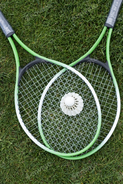 Preview: top view of shuttlecock on badminton rackets lying on green grass