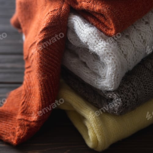 Preview: Cozy sweaters in autumn colors on brown wooden background.