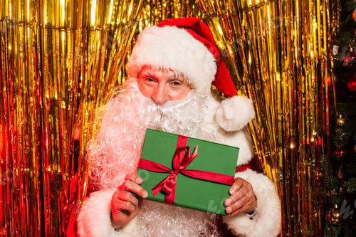 Preview: Father christmas in hat holding gift with bow near shiny tinsel