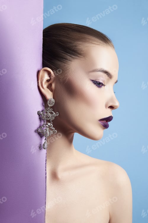 Preview: Earrings and jewelry in ear of a sexy woman pressed against the paper purple. Perfect brunette girl