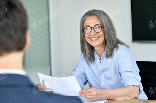 Preview: Happy female ceo listening colleague holding papers documents at table meeting.