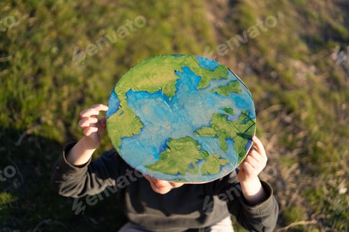 Preview: Little boy holding planet in hands against green spring background. Earth day