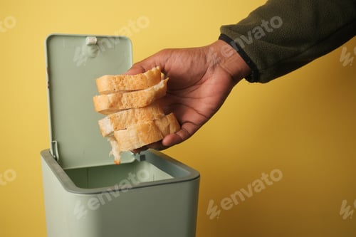 Preview: Hand disposing of stale bread in a green trash can