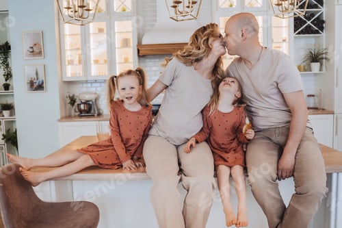 Preview: Family sits on kitchen table home, parents kissing each other while little daughter looking at them