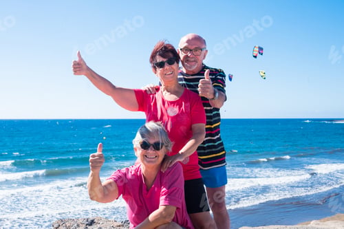 Preview: Three senior people in friendship enjoying the outdoors at sea gesturing ok sign with hands.