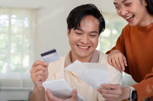 Aperçu: Happy couple celebrating their financial planning, reviewing bills and credit card together.