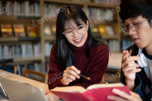 Preview: Glasses asian woman student pointing pencil at book man friend holding while sits at library's table