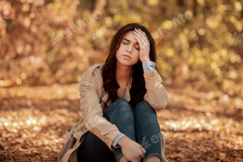 Preview: Tired or depressed young woman touching her head at autumn park