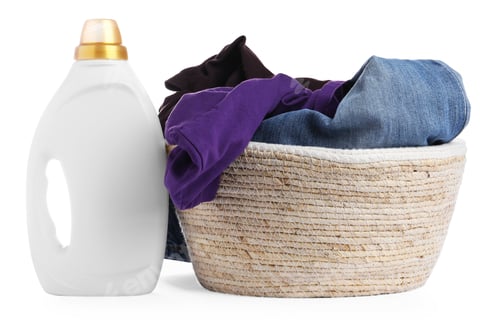 Preview: Bottle with fabric softener and basket full of clothes isolated on white