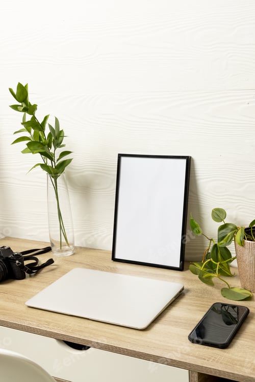 Preview: Vertical of black empty frame with copy space, plants, phone and laptop on table against white wall