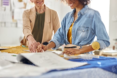 Preview: Professinal dressmaker with African-American colleague work with sewing patterns at cutting table