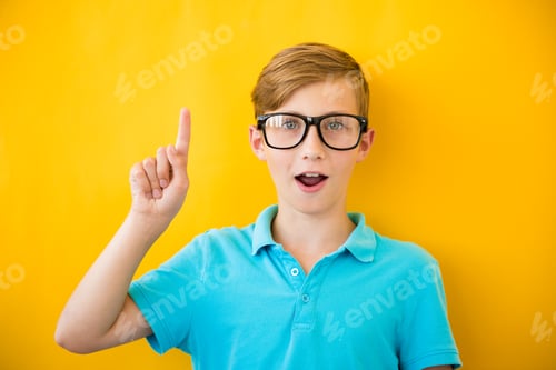 Preview: Portrait of stylish little boy with finger pointed up. Kid on yellow blackboard