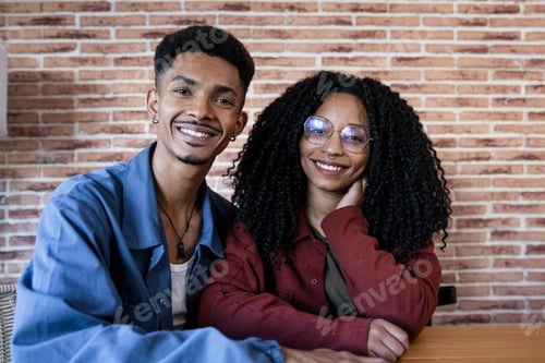 Preview: Young adult diverse smiling couple sitting at home looking at camera. Happy relaxed man and woman