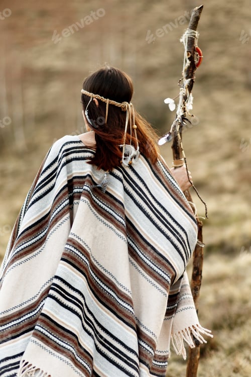 Preview: beautiful native indian american woman holding pikestaff and walking in mountains in evening