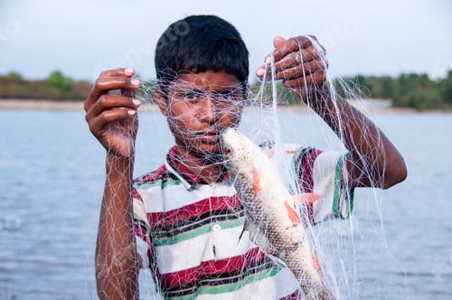Preview: Young Fisherman take fish out of the net in front lake, India.