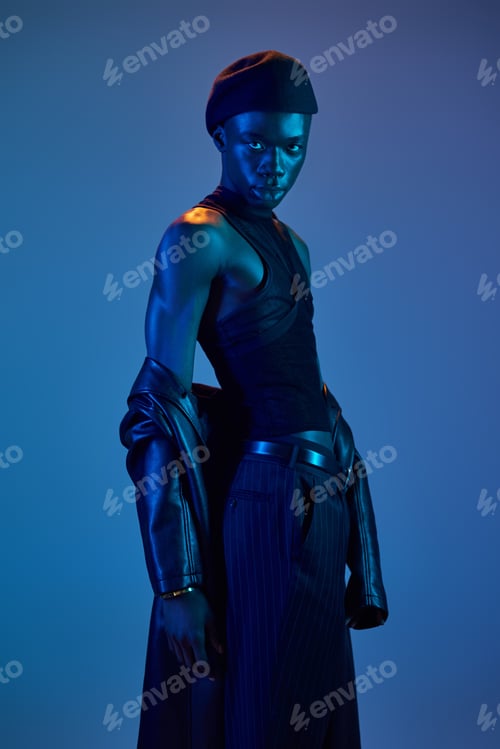Preview: Stylish young man exuding confidence in vibrant blue lighting with striking attire