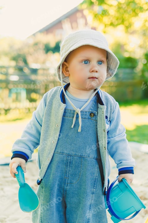 Preview: Toddler playing with a shovel in the sandbox on the playground. Boy playing in nature. 2 year old